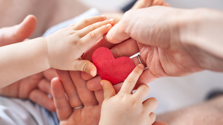 baby naming ceremony, parents holding baby's hands and a paper heart