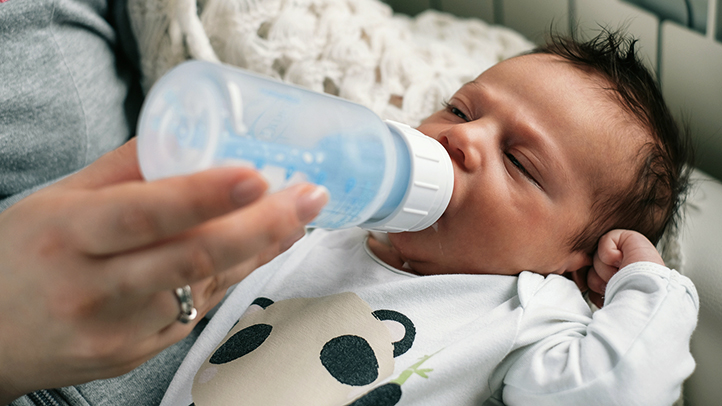dream feeding baby, baby being bottle-fed with eyes closed