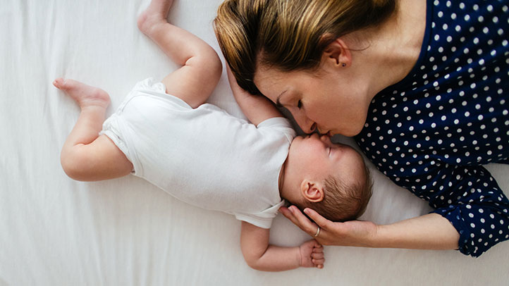 mom kissing sleeping baby in bed, pillow for baby
