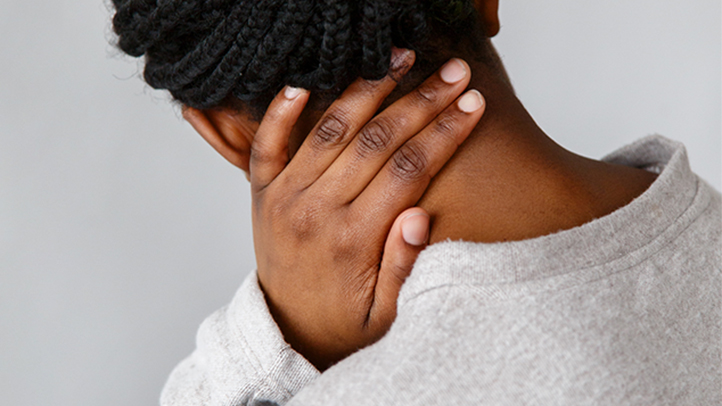 postpartum back pain, woman rubbing the back of her neck with her hand