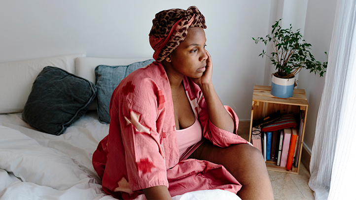 woman sitting on bed with legs crossed staring out the window, postpartum perineal pain