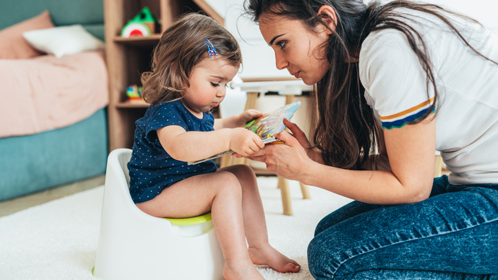 resisting potty training, little toddler girl on the potty with her mom reading her a story