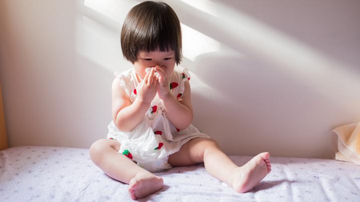 when your toddler has an object stuck in the nose, little toddler girl blowing and touching her nose on a bed